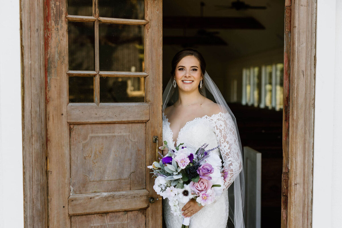 bridal portrait of bride in white wedding gown standing inside chapel doors at Four Fifteen Estates in New Boston, TX