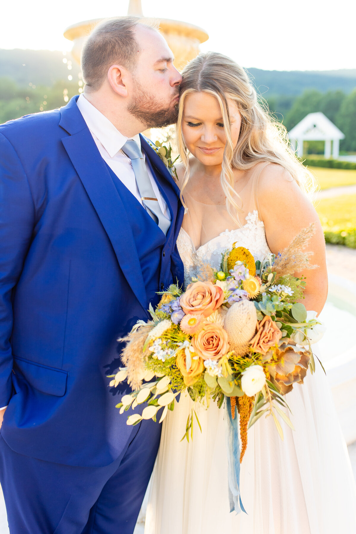 Groom kissing the bride gently on the side of the head as she holds her bouquet