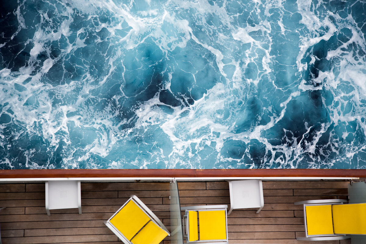 The view of the ocean, with white caps, from a cruise ship balcony that is lined with yellow chairs.