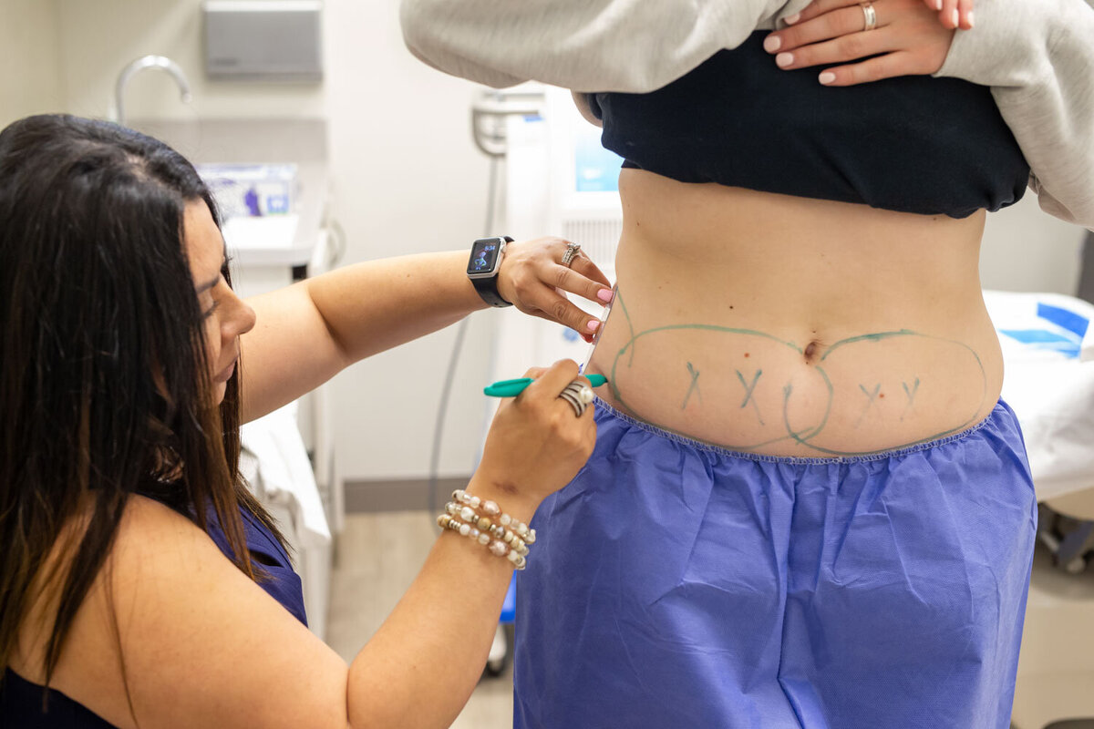 A woman is drawing circles on a woman 's stomach with a marker