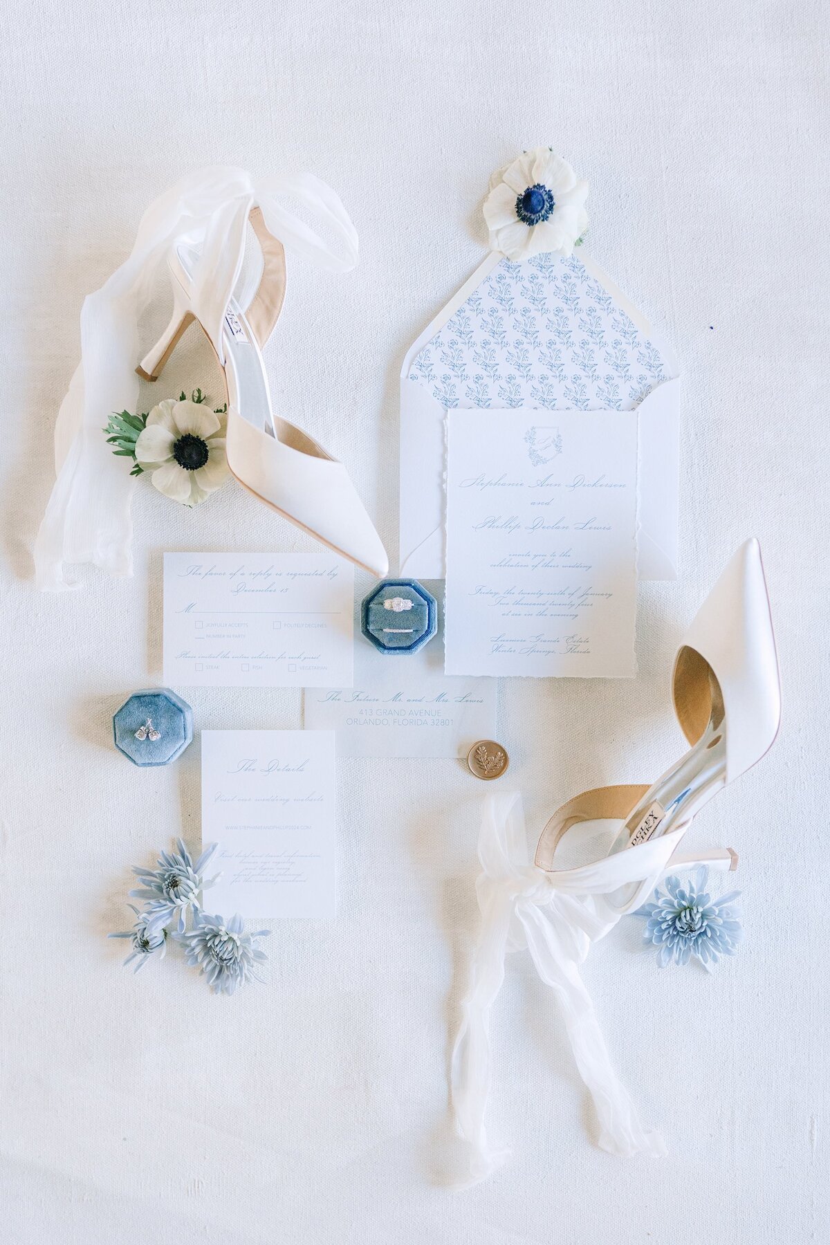 Blue and white wedding invitation suite styled with white heels and soft florals.