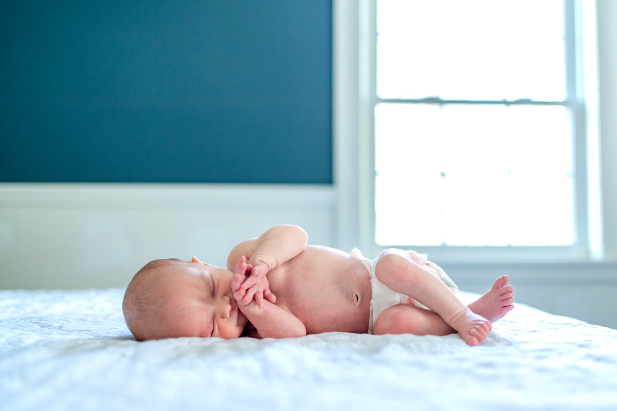 Baby laying on parent's bed in front of window and blue wall