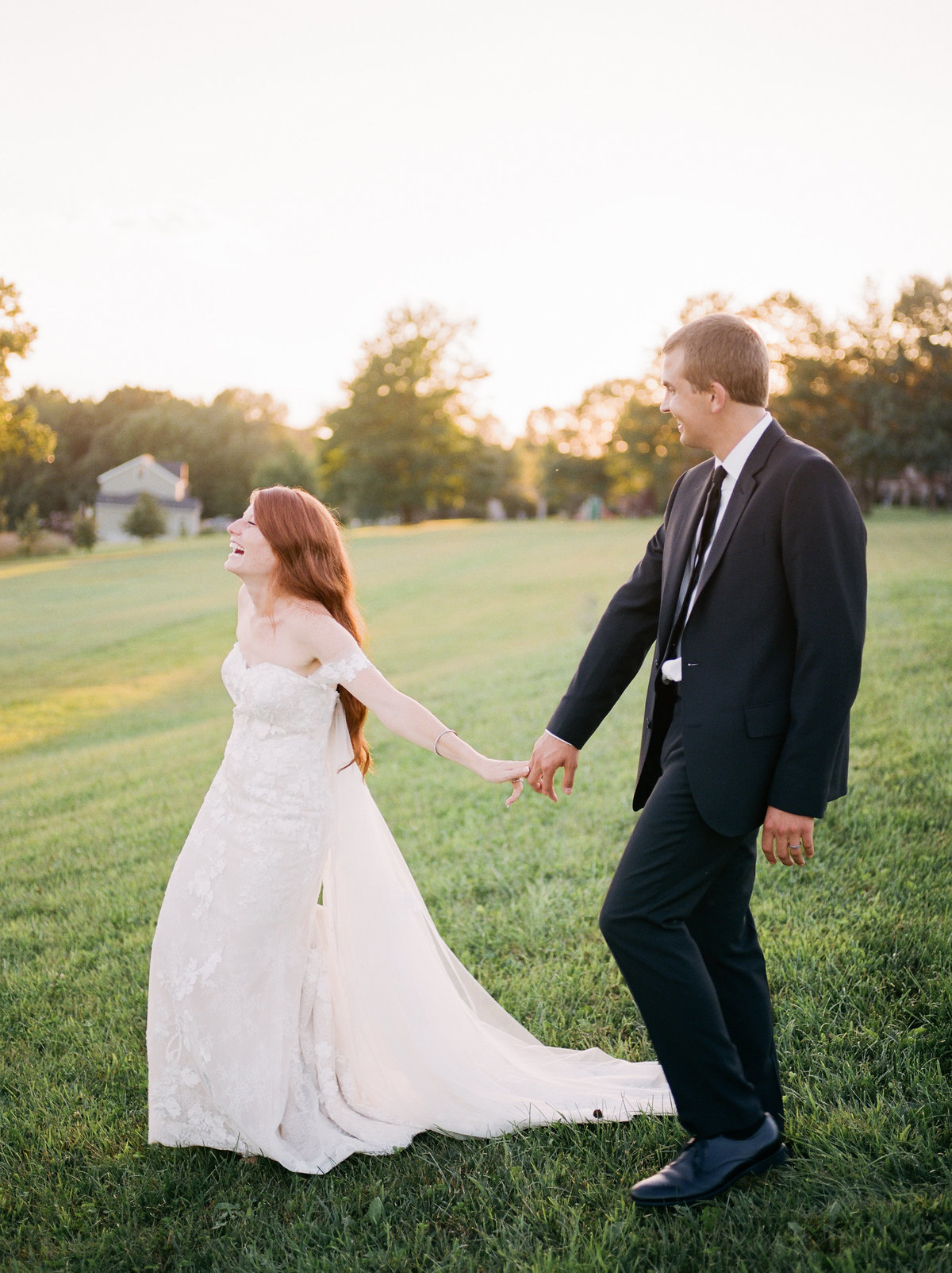 bride and groom holding hands and walking through grassy field