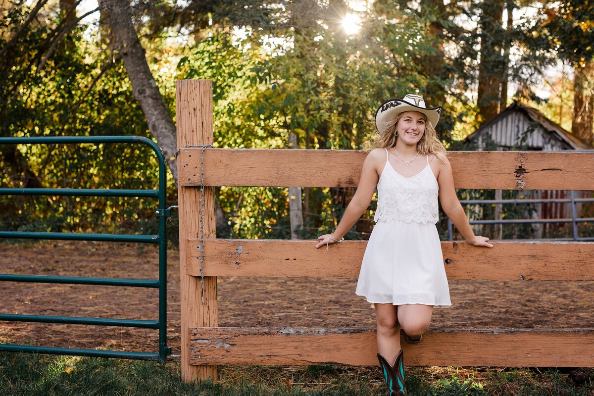 A high school senior girl standing in front of a horse pen.