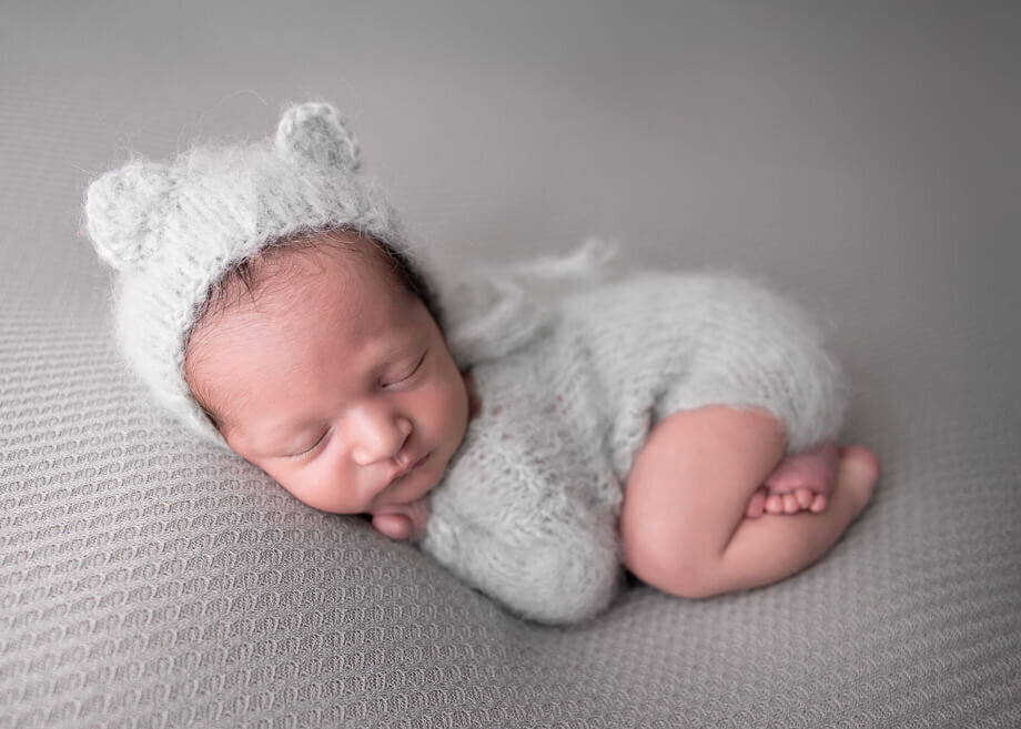newborn baby boy on sage green backdrop.  He is posed bum up and is wearing a mohair outfit with a matching bear bonnet