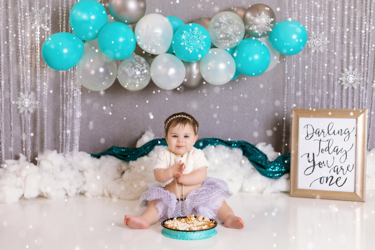 Cake Smash Photographer, a baby sits with cake and a sign that reads "Darling, today you are one"