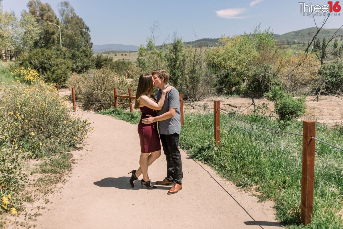 Engaged couple stop along a trail at Peters Canyon Regional Park for a kiss