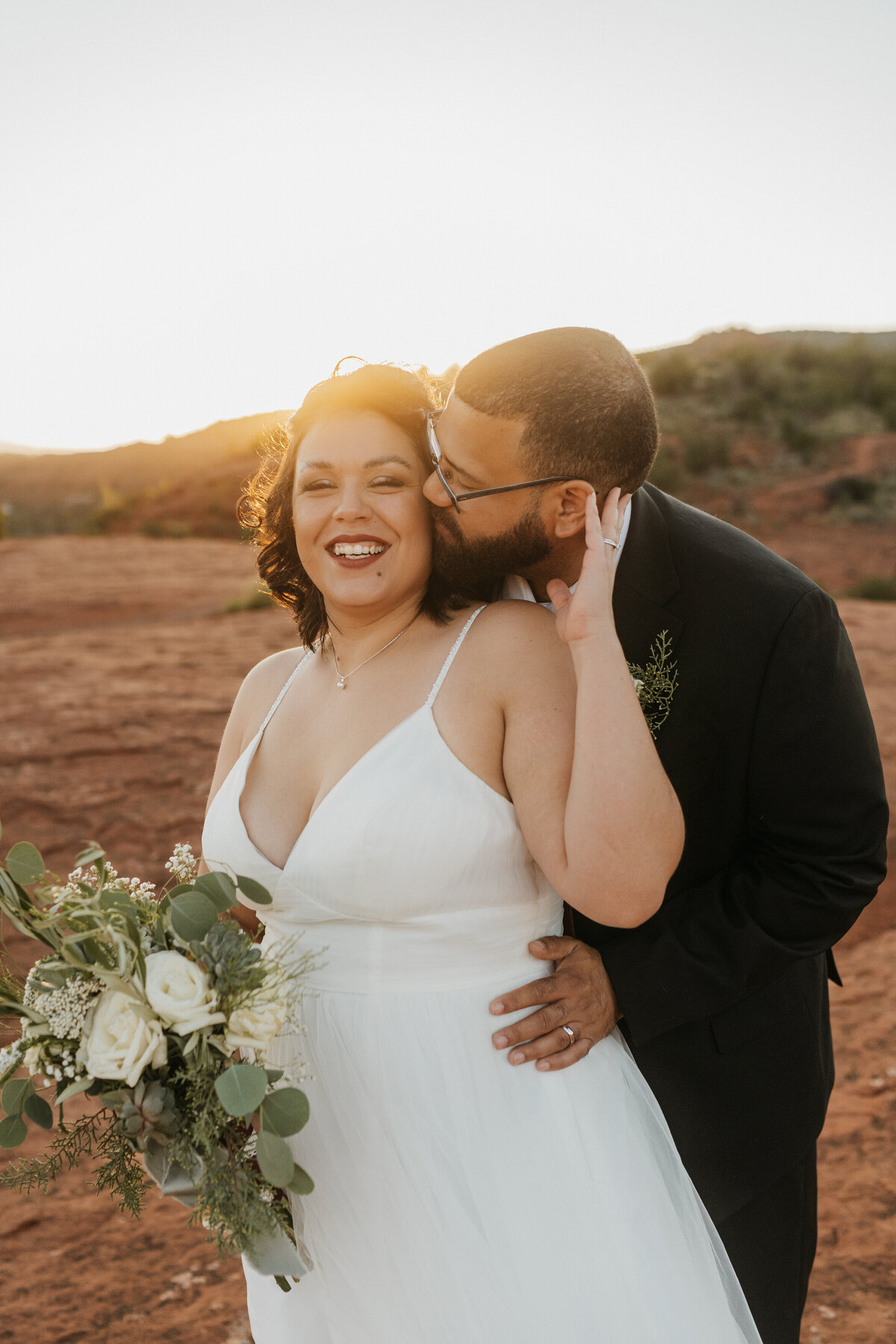 A person standing behind their partner and kissing their cheek 