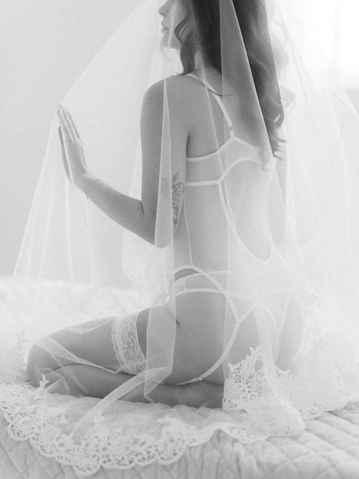 black and white photo of woman under bridal veil in a white lingerie set moves hand out in seattle bridal boudoir photography by Jacqueline Benét 