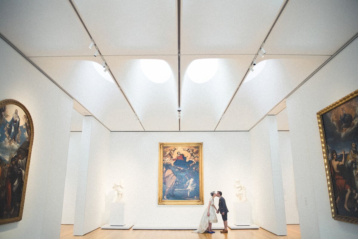 A wedding couple kissing in a brightly lit museum.