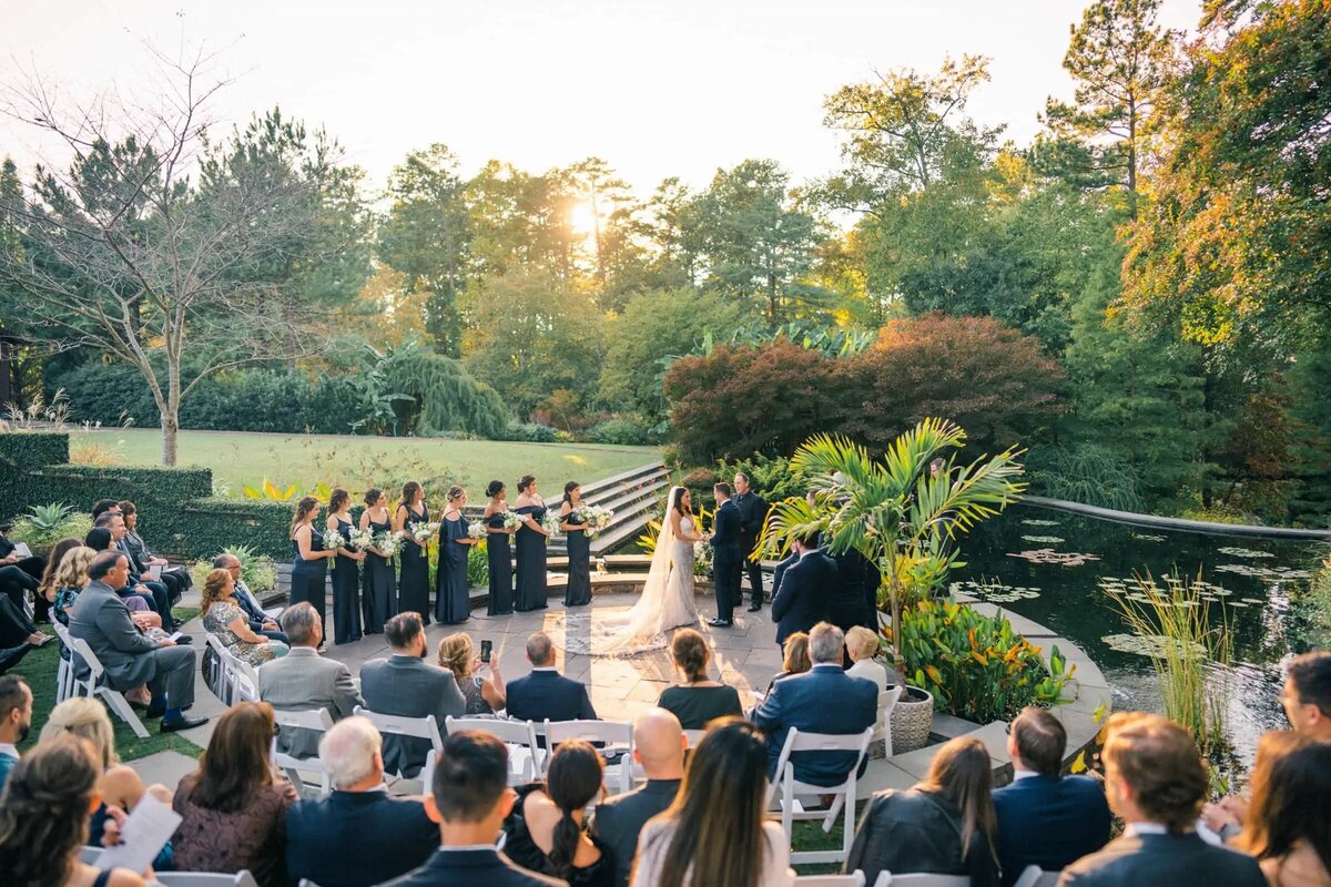 Outdoor wedding ceremony at Duke Gardens with guests seated around a reflective pond, surrounded by lush greenery
