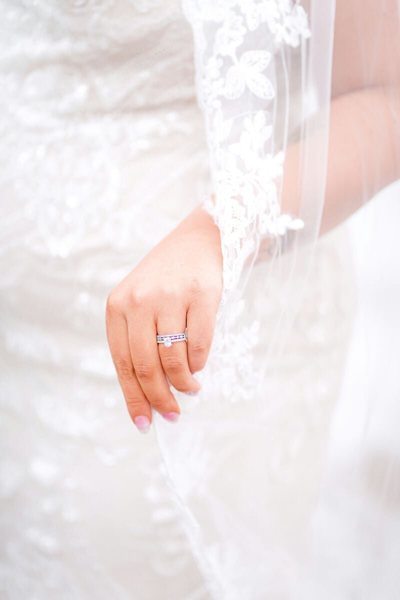 Close-up of a bride's hand holding her lace veil, showcasing a beautiful wedding ring.