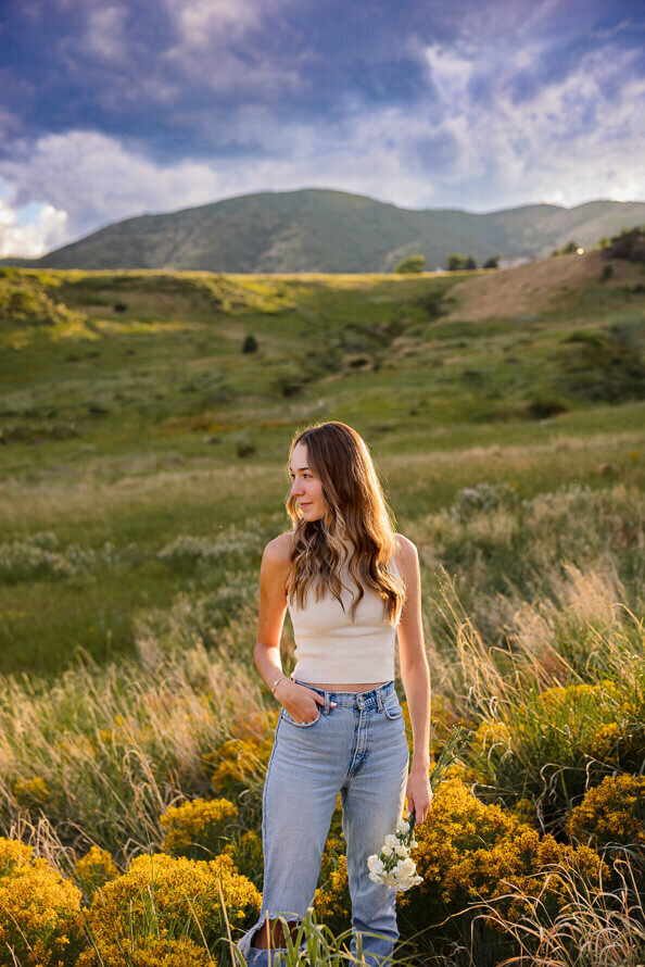 Girls puts hand in pocket and hold flowers with green mountains behind her.