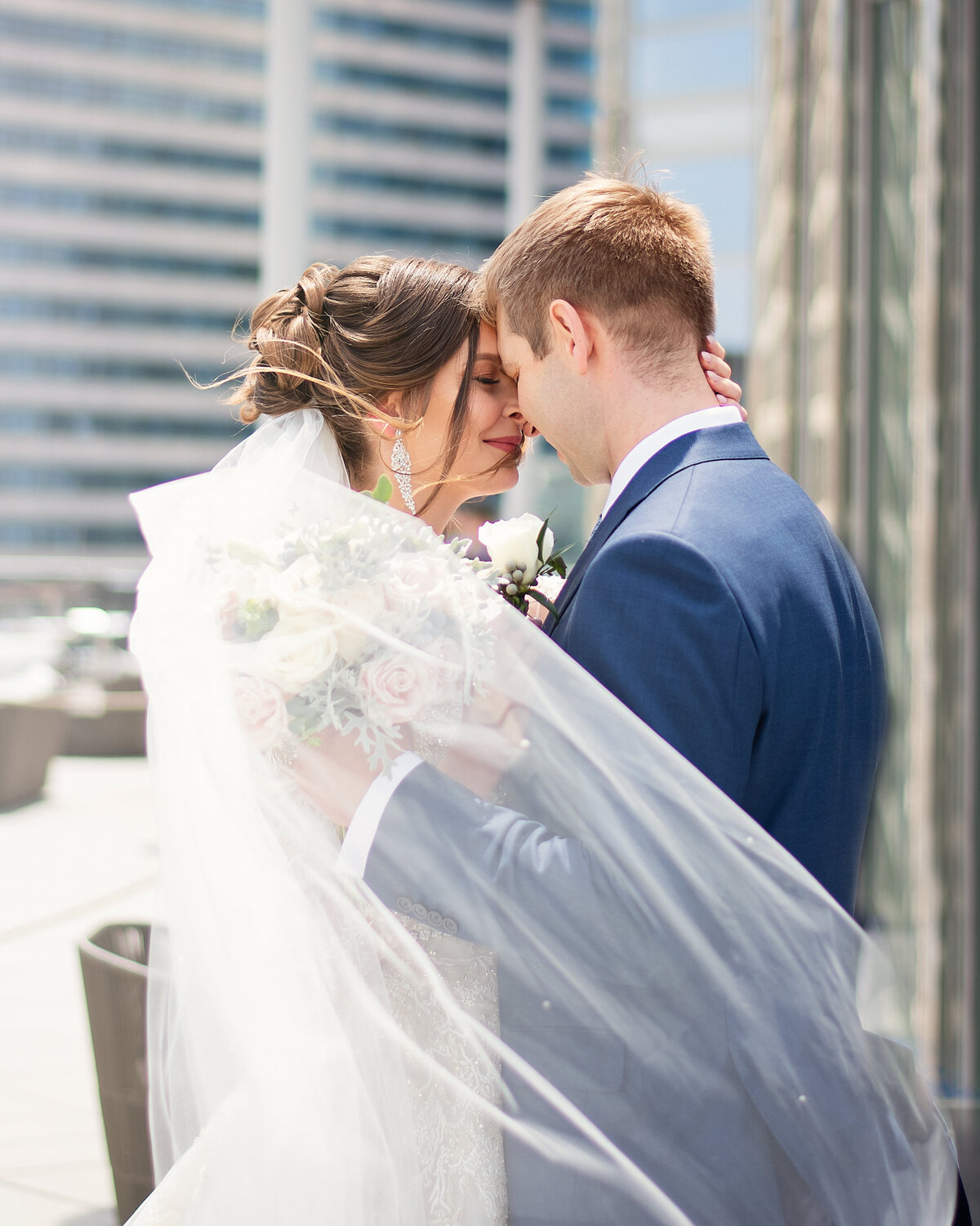 bride and groom touching  foreheads together  on the Trump hotel rooftop while the wind is blowing the long veil