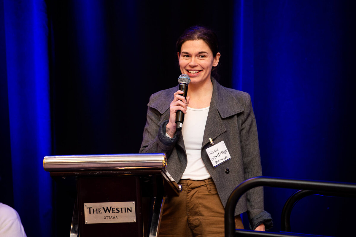 Ottawa event photos showing a female speaker in a grey jacket addressing attendees during a corporate conference at the Westin Hotel.  Captured by JEMMAN Photography COMMERCIAL