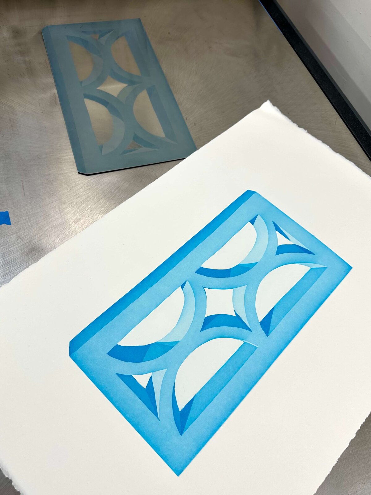 A clean aquatint print in shades of sky blue rests beside its etched copper plate, still on the press bed.