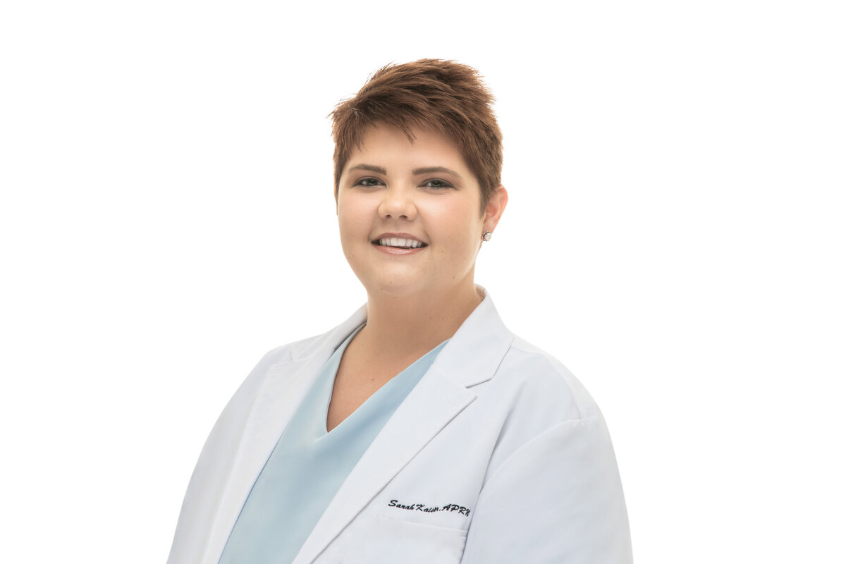 A woman female medical professional nurse practitioner with short dark hair poses for a professional headshot in a white lab coat on a white background for Janel Lee Photography studio Cincinnati Ohio