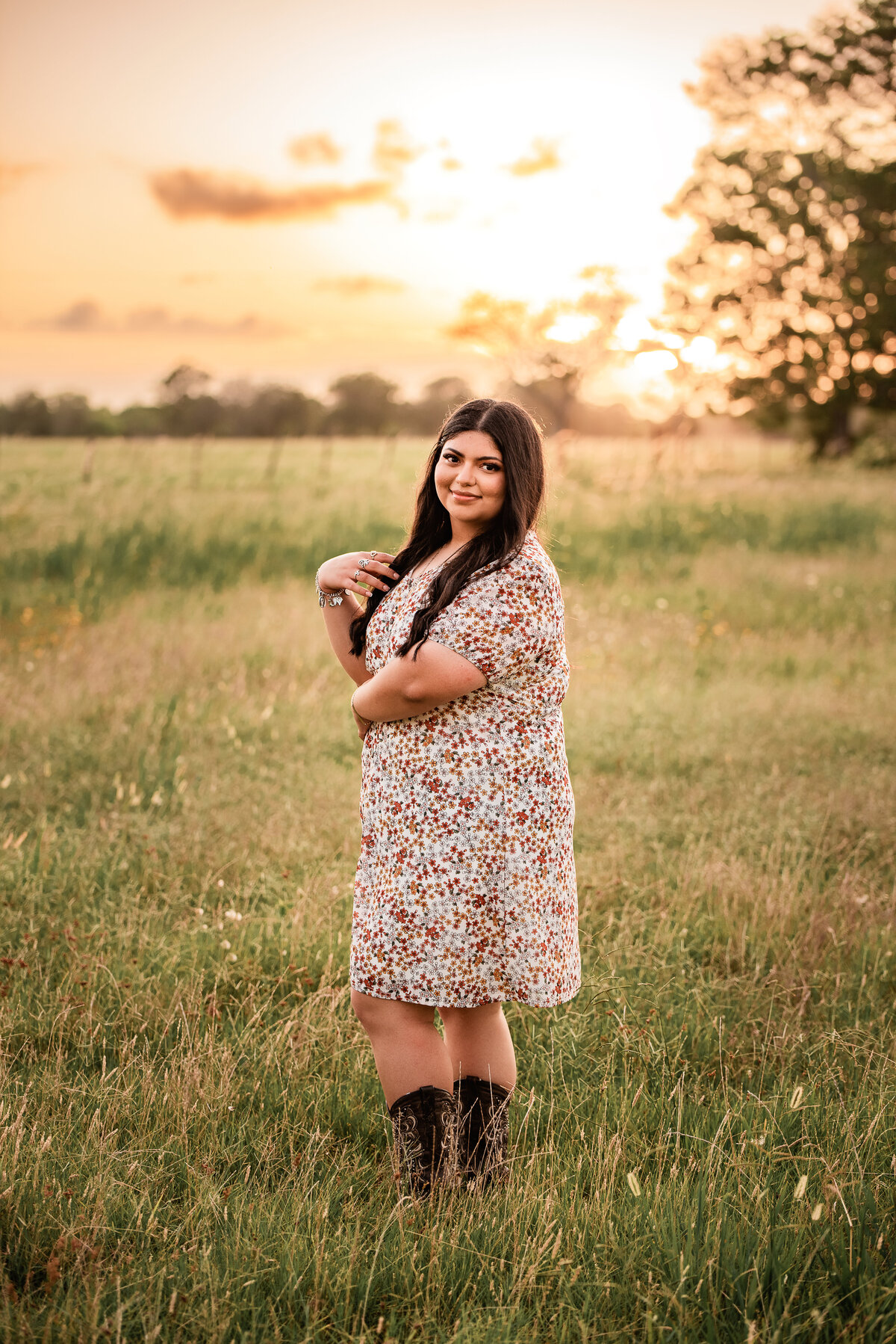 A Houston senior stands in a field wearing cowboy boots and a floral dress.