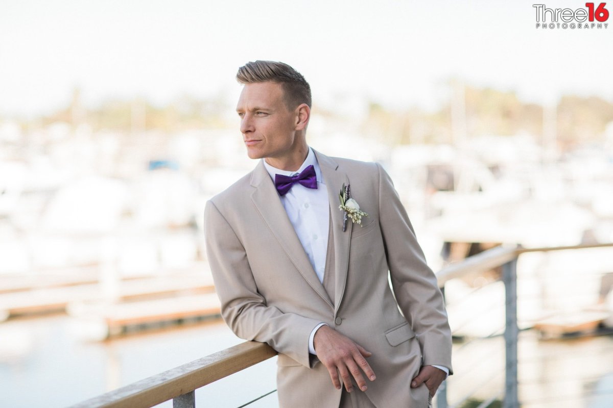 Groom poses as he leans on patio rail looking out towards the beach
