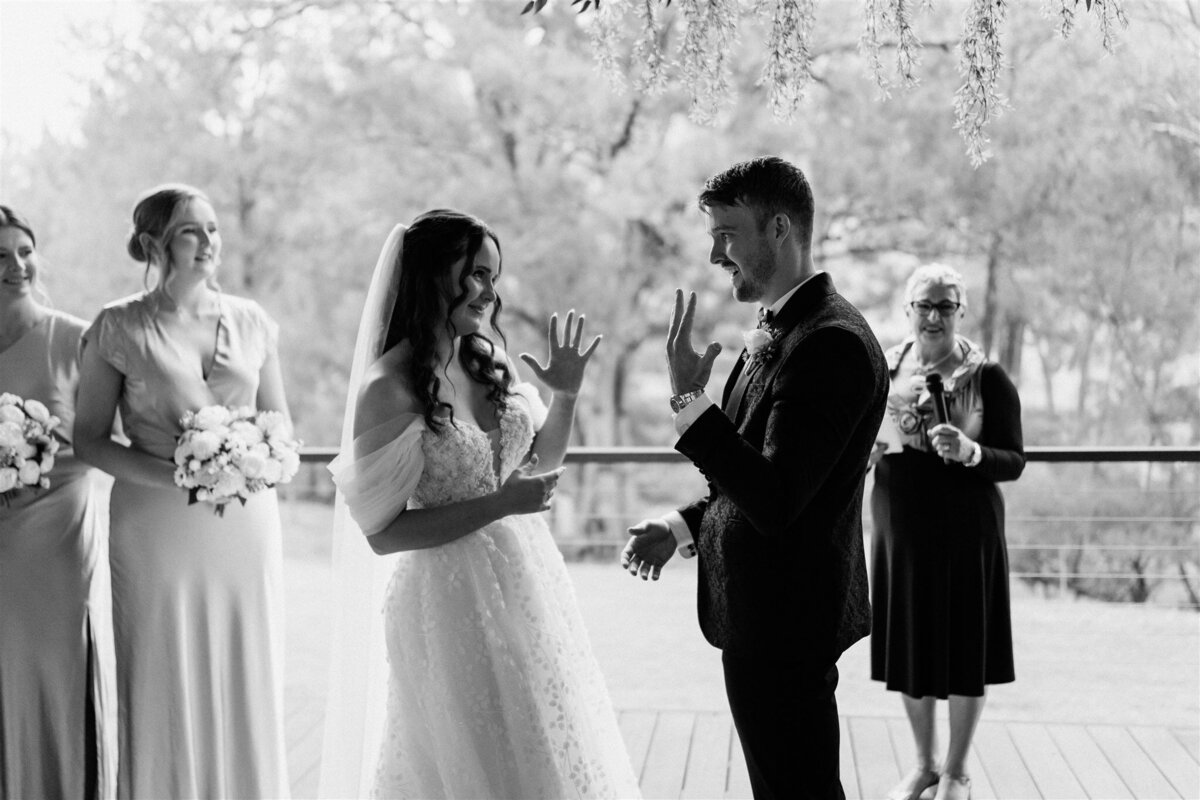 The bride and groom, standing beneath a canopy of flowers, exchange heartfelt vows as tears glisten in their eyes.