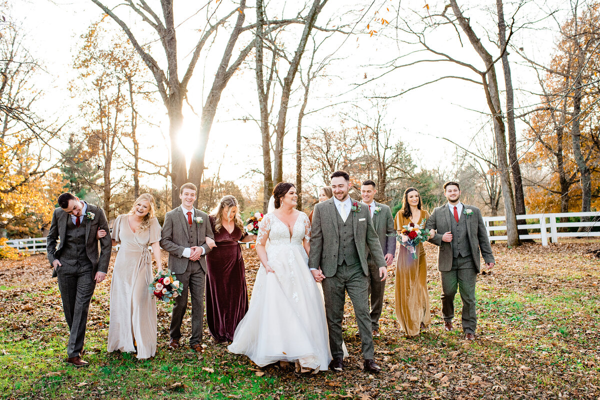 Wedding party wearing shades of autumn colors, men are wearing tweed suits and they are strolling through an open field at golden hour