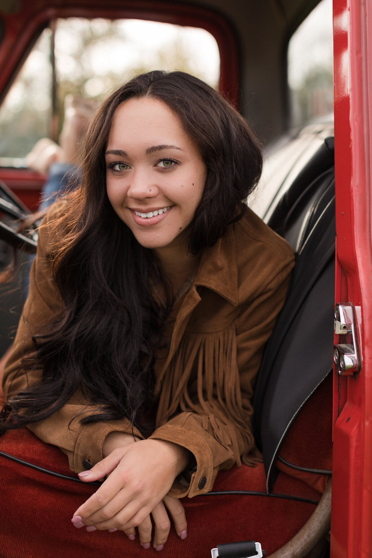 Senior girl laying across the front seat of an old truck smiling at the camera