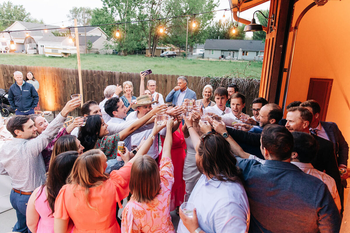 A group of people holding their glasses together in a toast at an outdoor wedding reception.