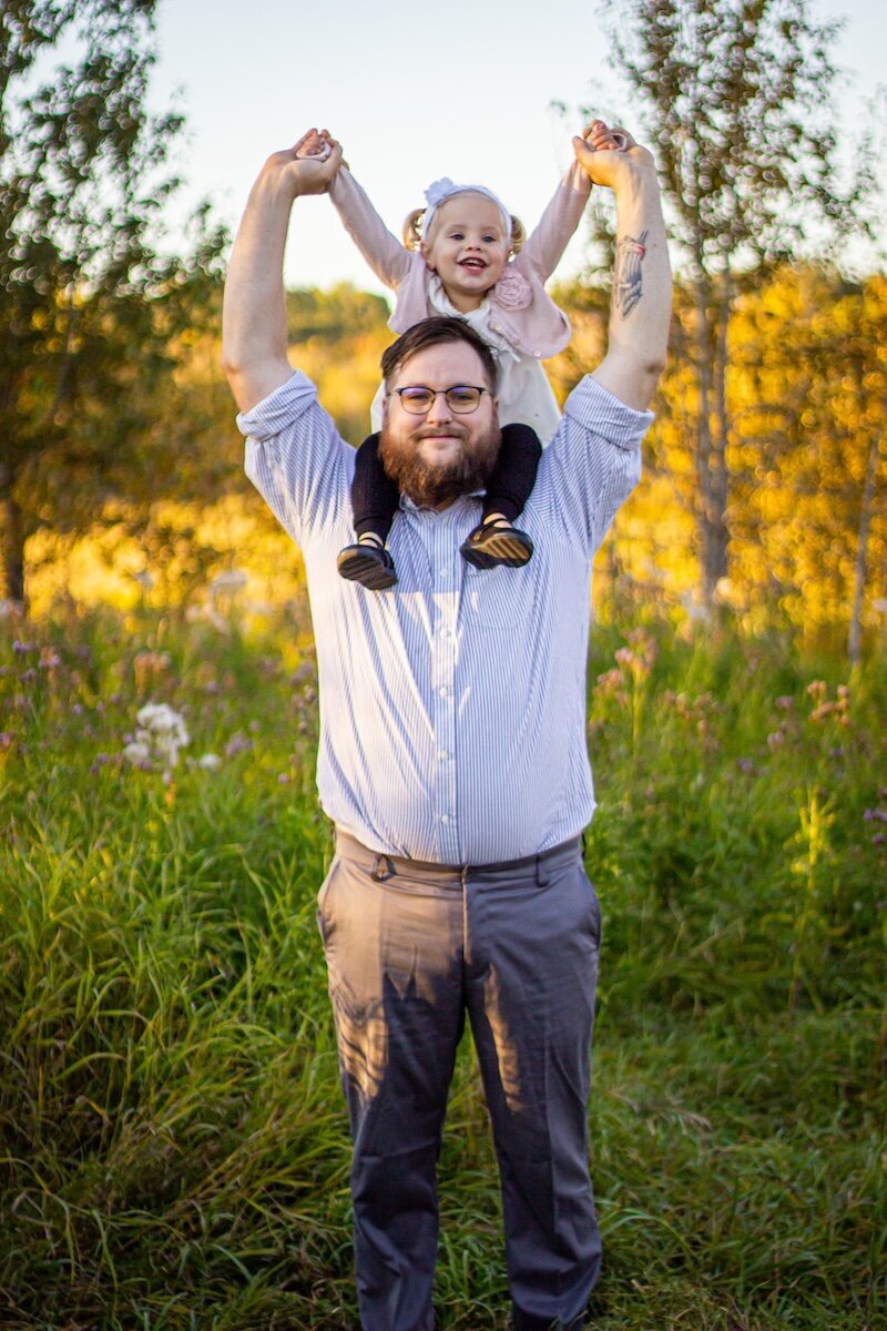 a father holds his daughter on his shoulders near Edmonton