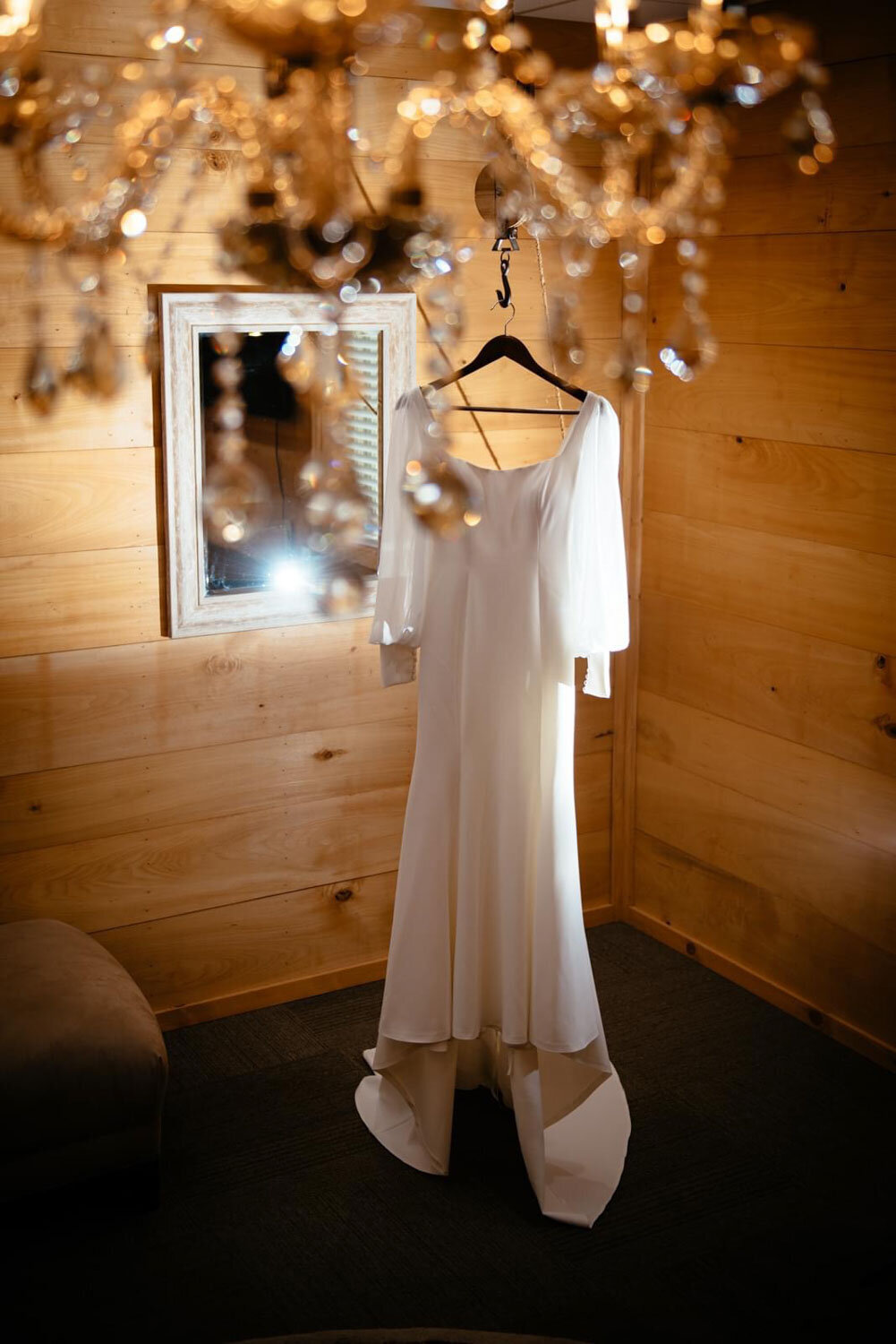 Wedding gown hanging under a chandelier in a rustic, wooden room