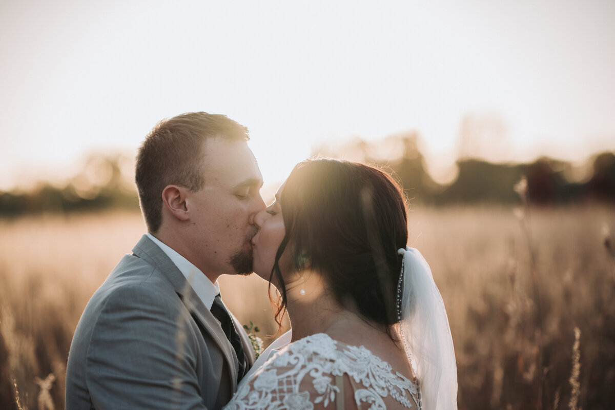 Bride and groom sharing a kiss at sunset in a wheat field.