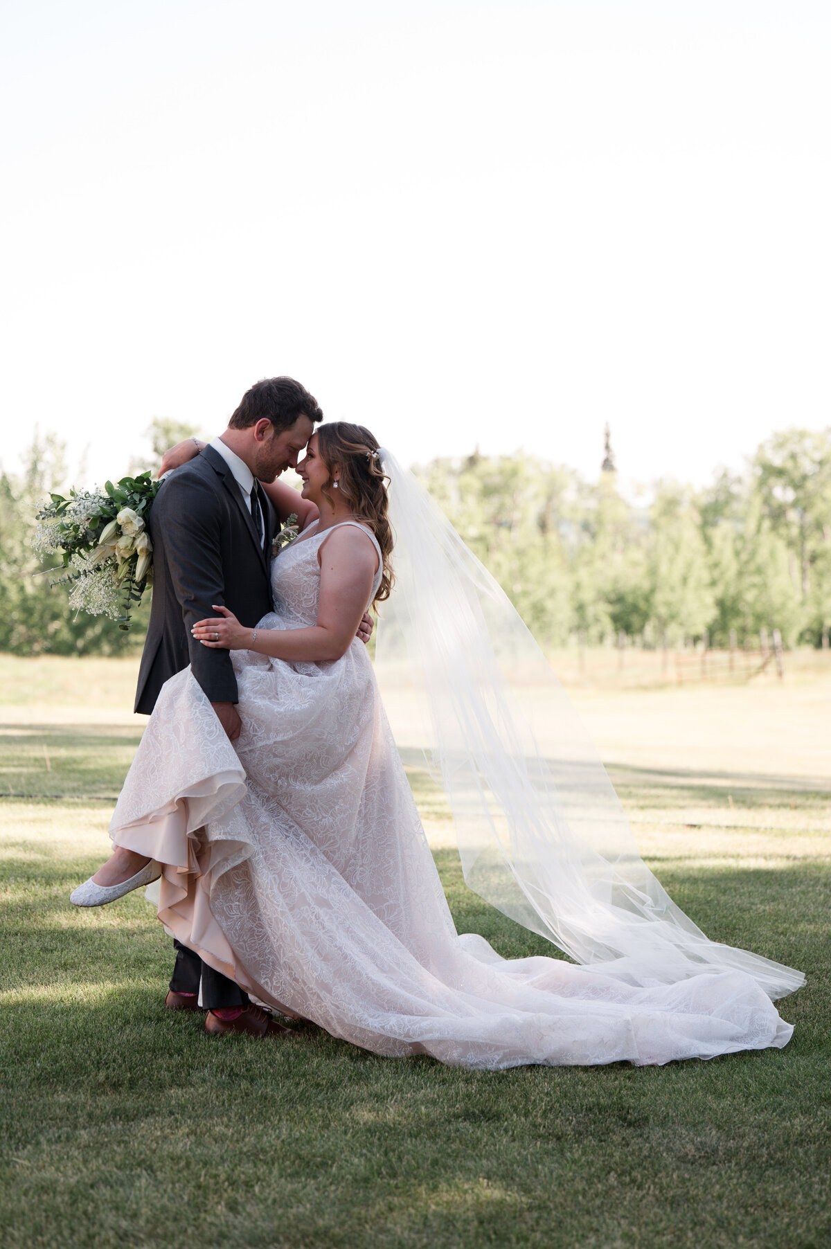 wedding couple standing close to each other, man leans down to kiss his bride