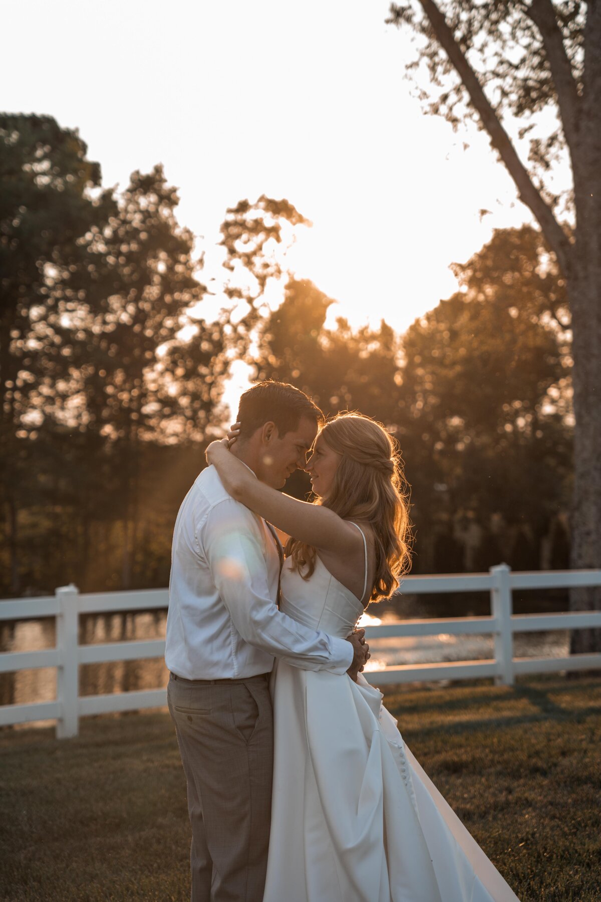 newlyweds embracing under a sunset in front of a white fence