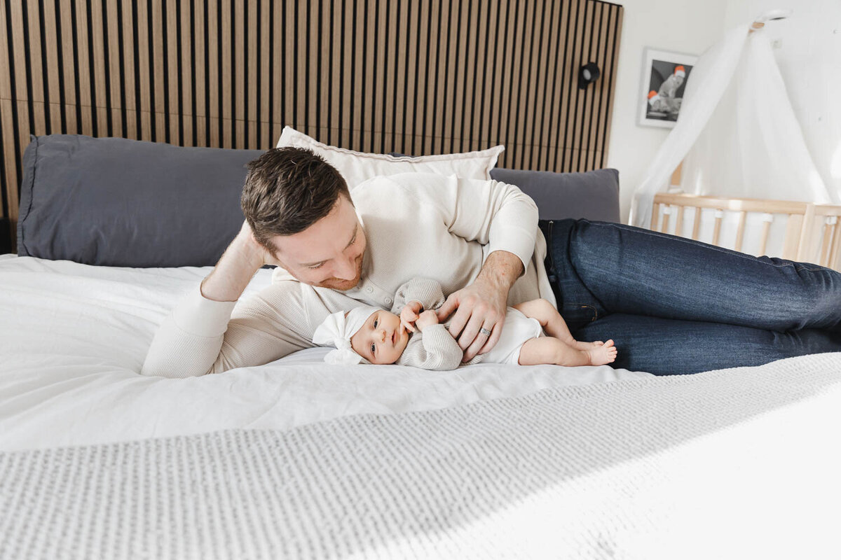 dad and newborn daughter laying on bed