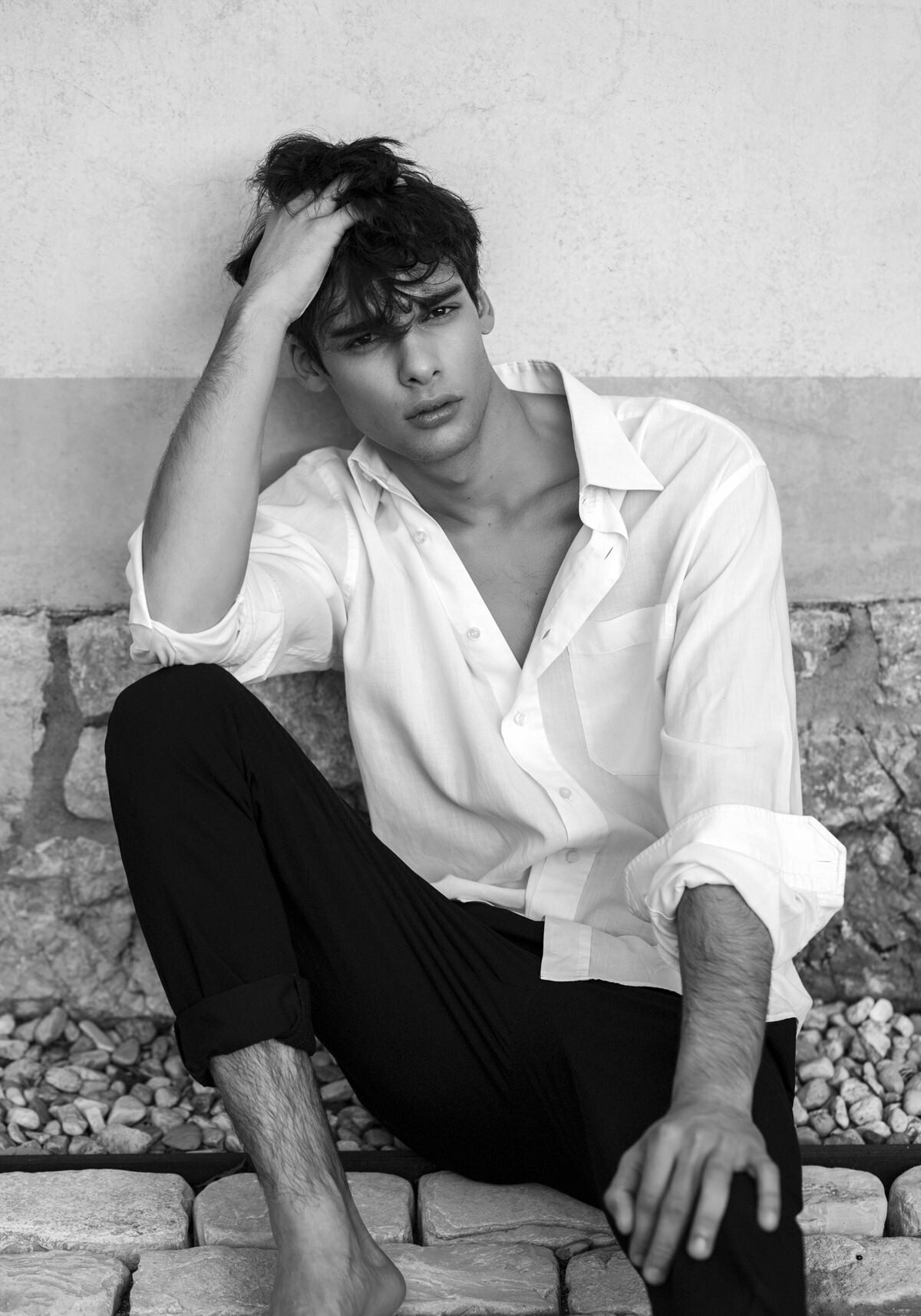 A black-and-white portrait of a young man with tousled hair, wearing a white button-down shirt