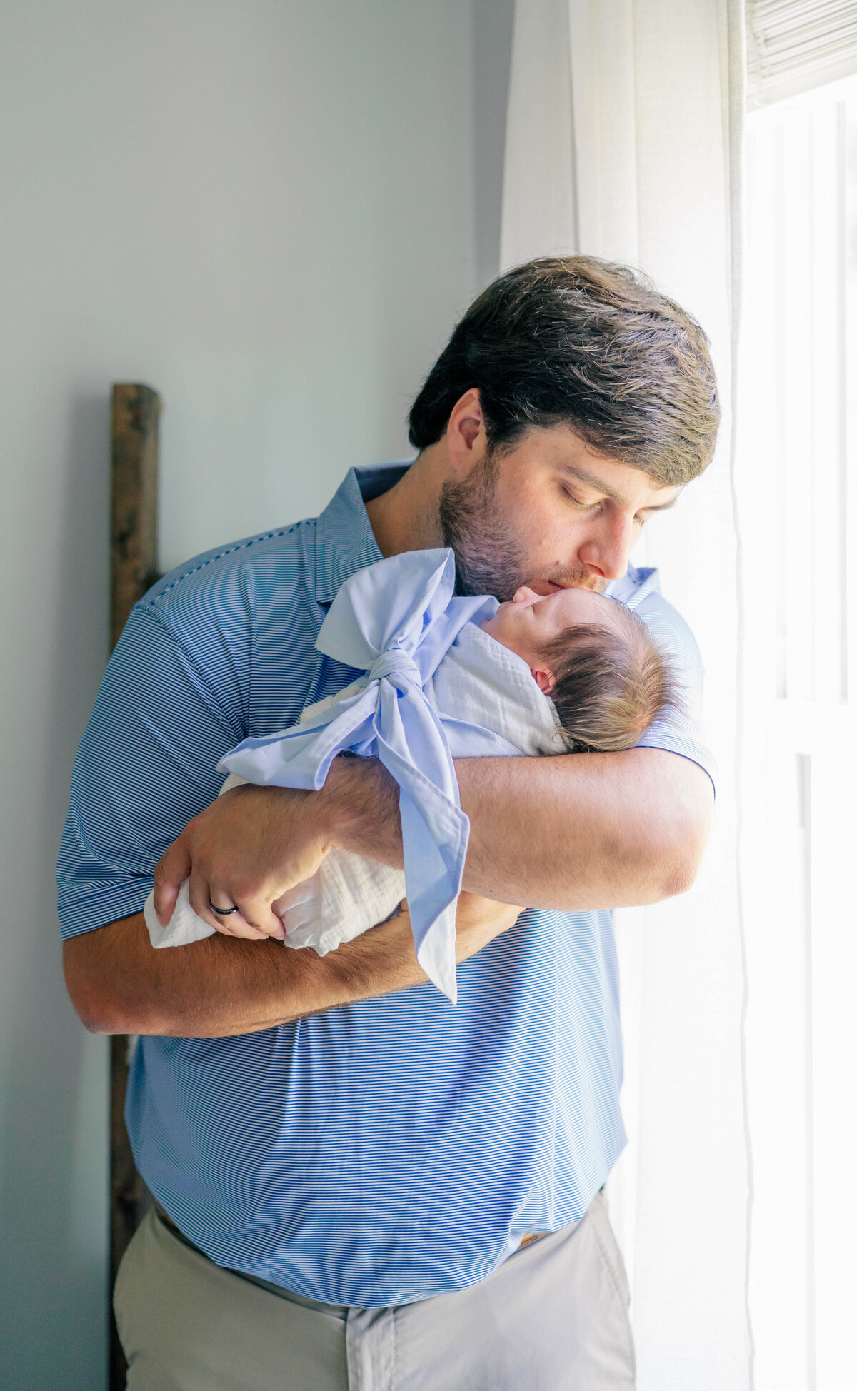 proud dad kissing sleeping newborn while wrapped in bow during their indoor newborn shoot