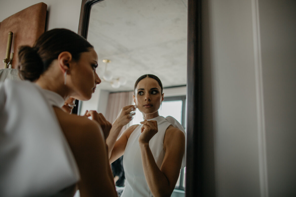 Bride putting earring in while looking into mirror