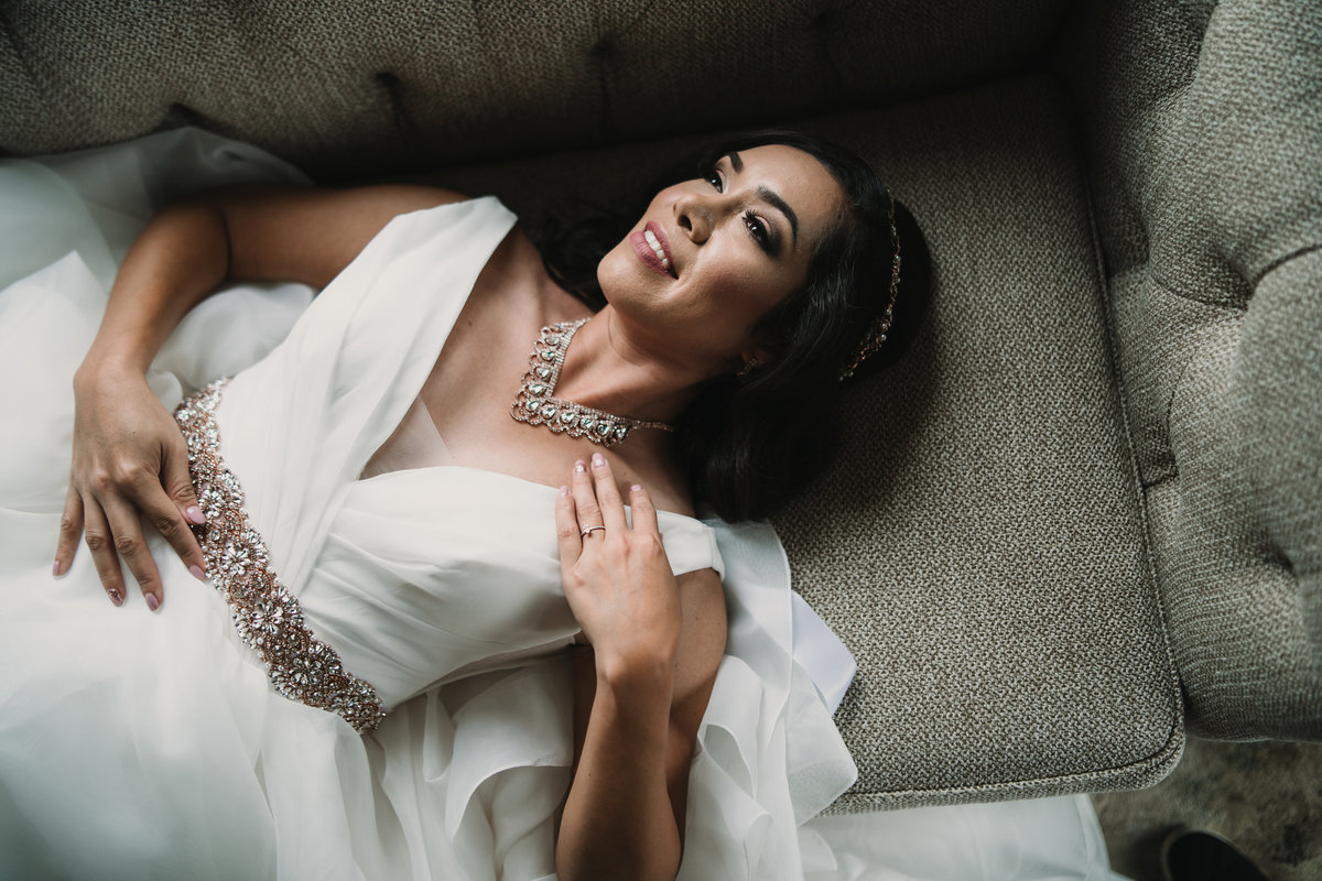 Bride laying on couch and posing for photographer for her bridal portrait