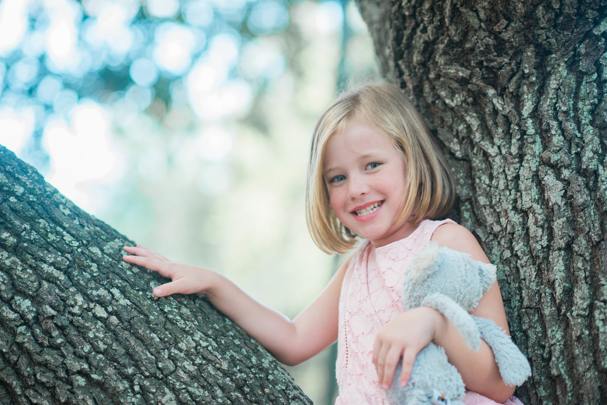little girl sitting in tree with stuffed animal