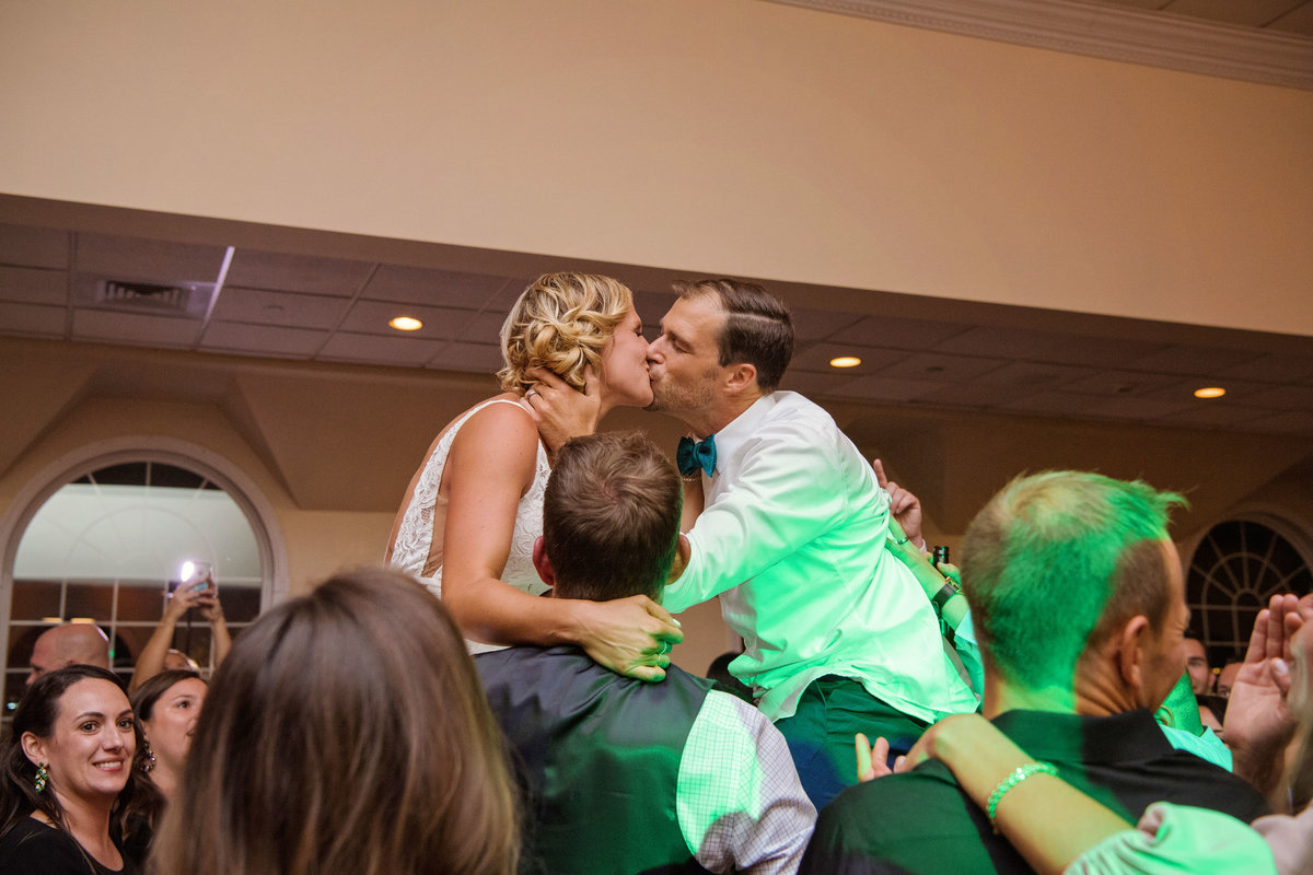Bride and groom kissing while being lifted in chairs at Captain Bills