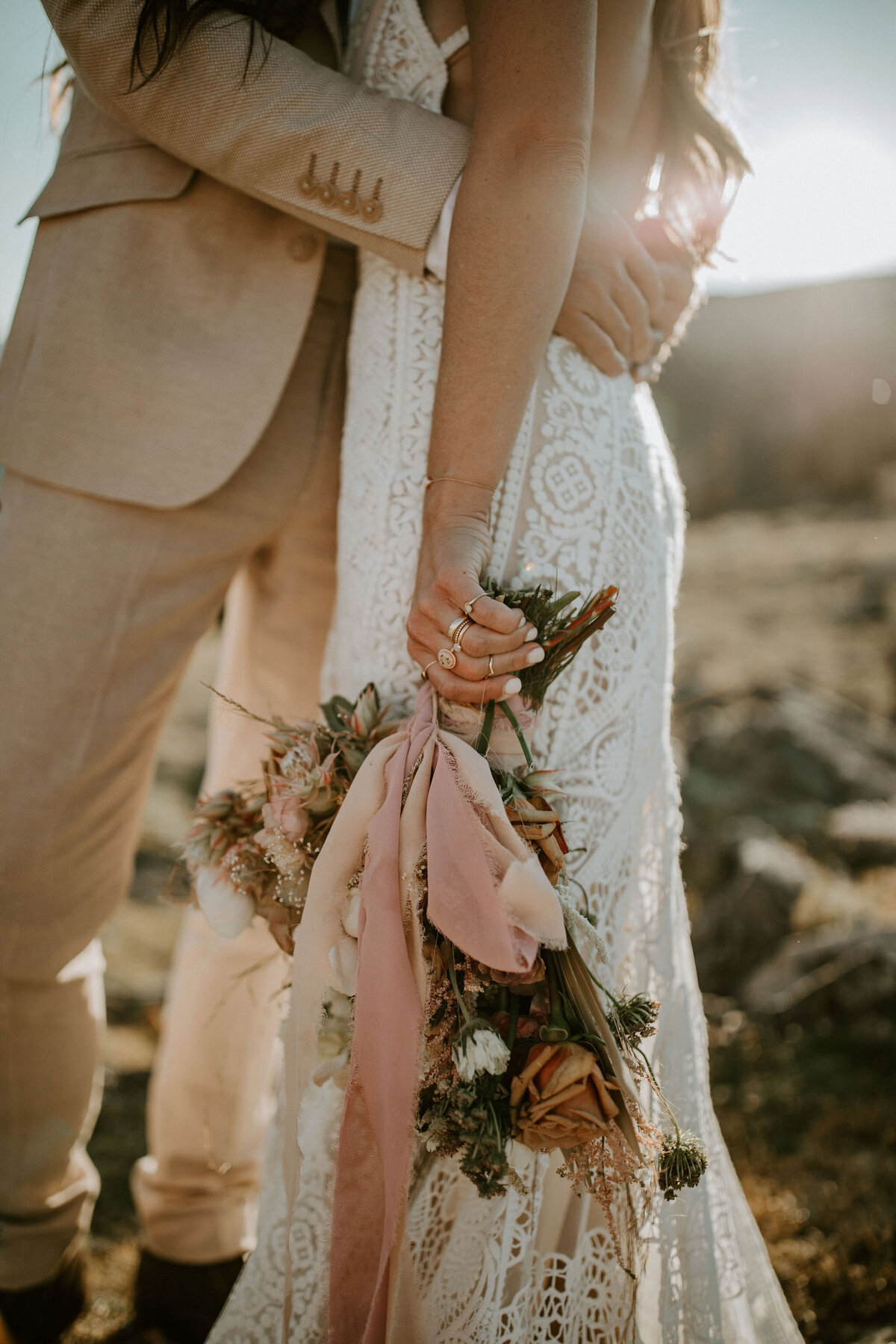 Closeup of bride and groom outdoors wearing an ivory suit and white wedding gown holding a bouquet of flowers.