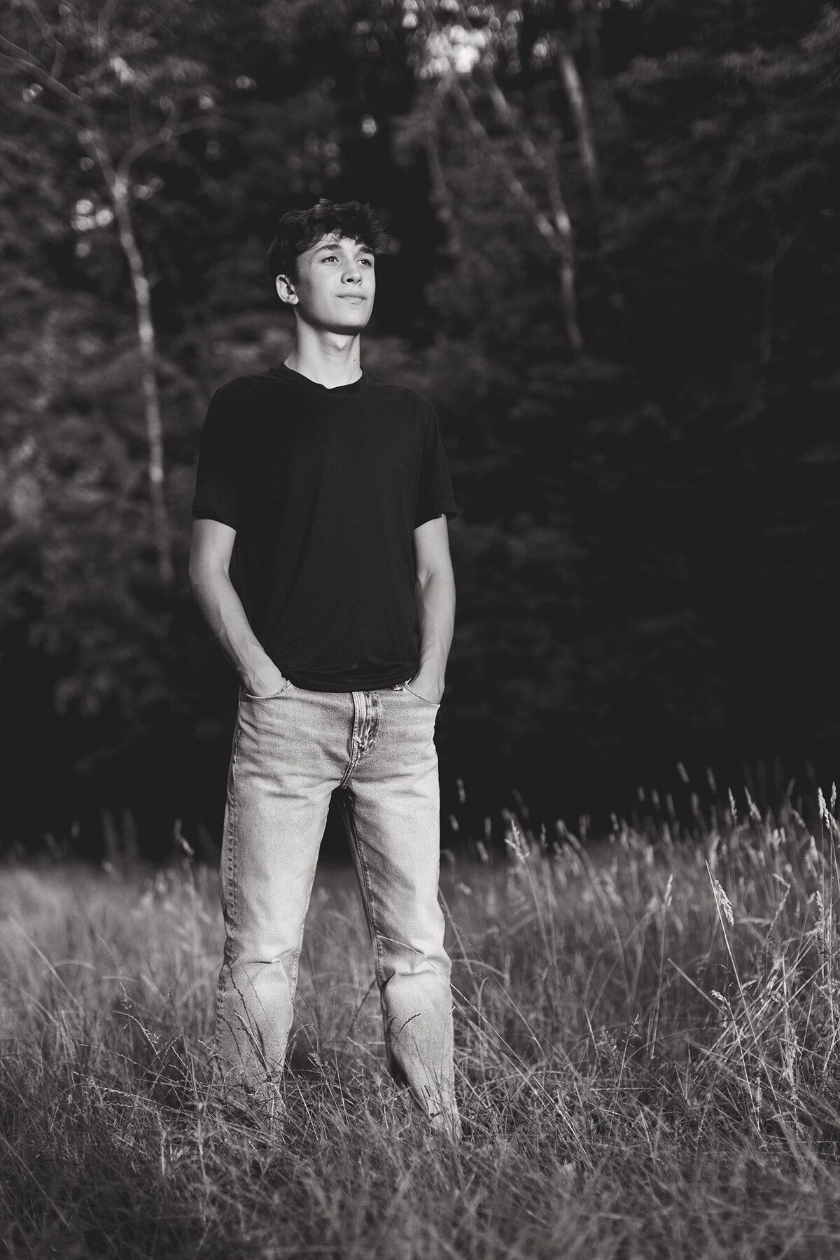 young man standing in jeans and a tshirt in a grass field for highschool senior pictures.