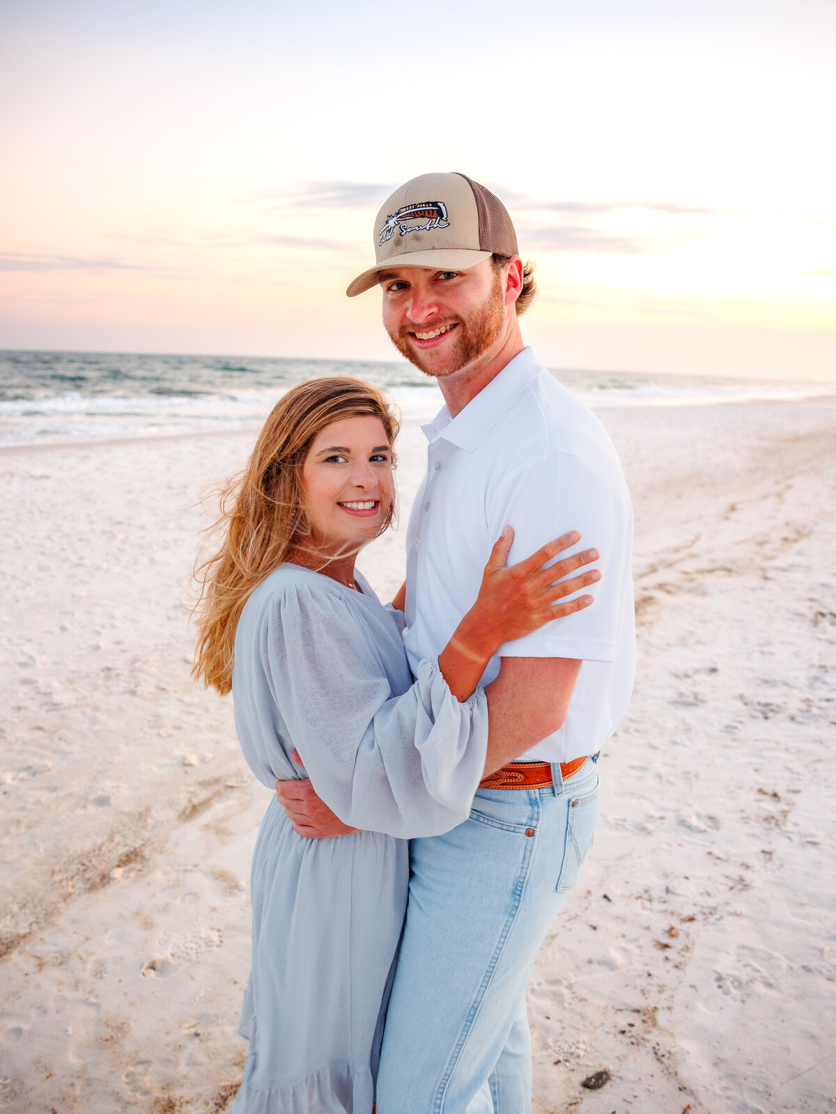 Couple faces each other in a standing pose with orange sunset behind them
