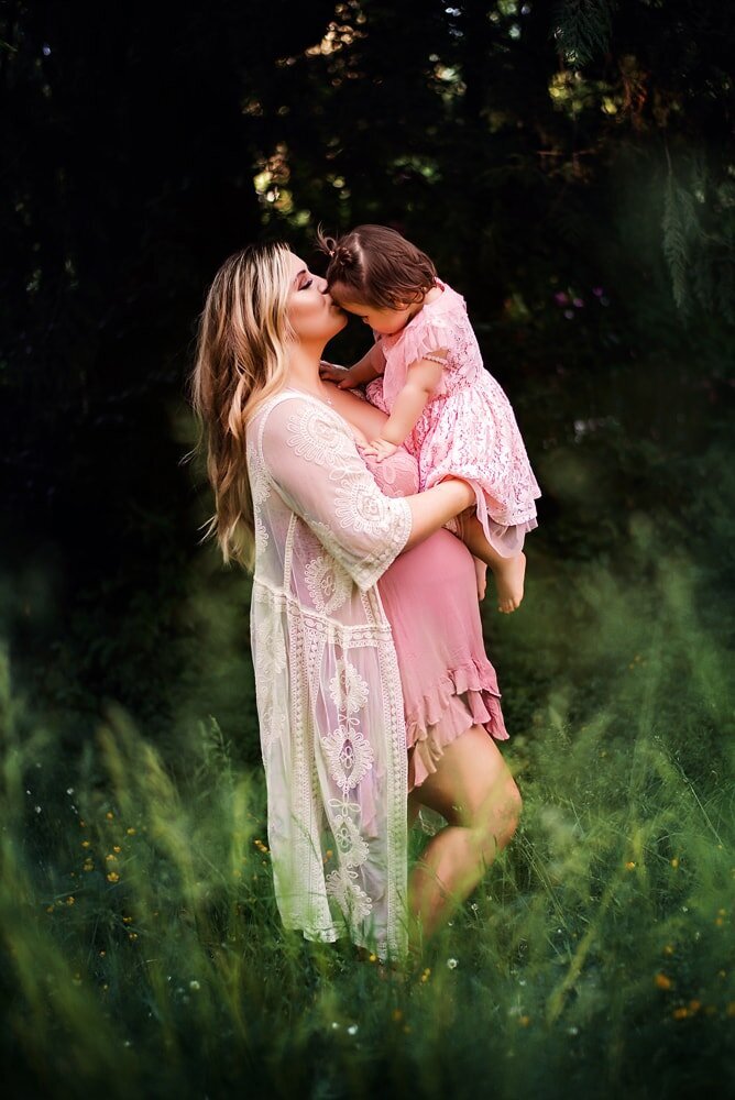 Pregnant mother and toddler daughter wearing boho pink dresses in long grass