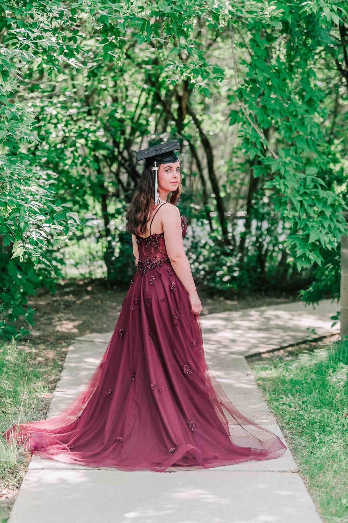 A young girl wearing a burgundy dress and a grad cap.