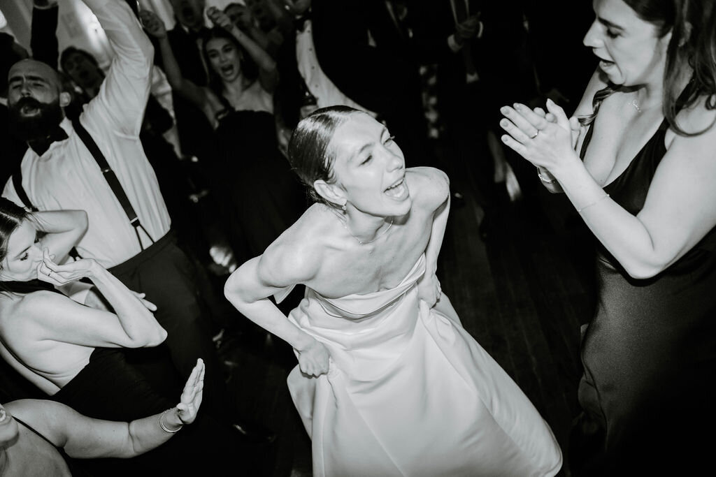 Rhode Island Wedding Photographers | Bride in white strapless gown laughing joyfully on a lively dance floor, surrounded by clapping guests