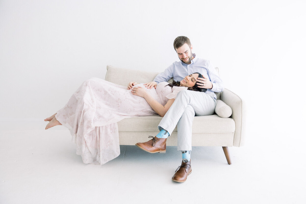 Pregnant woman laying on husband's lap holding belly for maternity photographer  in Tampa Tina Marie Studio.