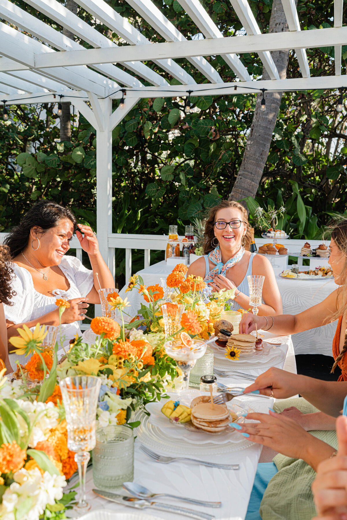 girlfriends at beach brunch the table is adorned with white, orange, blue and green floral table runner and buffet brunch foods
