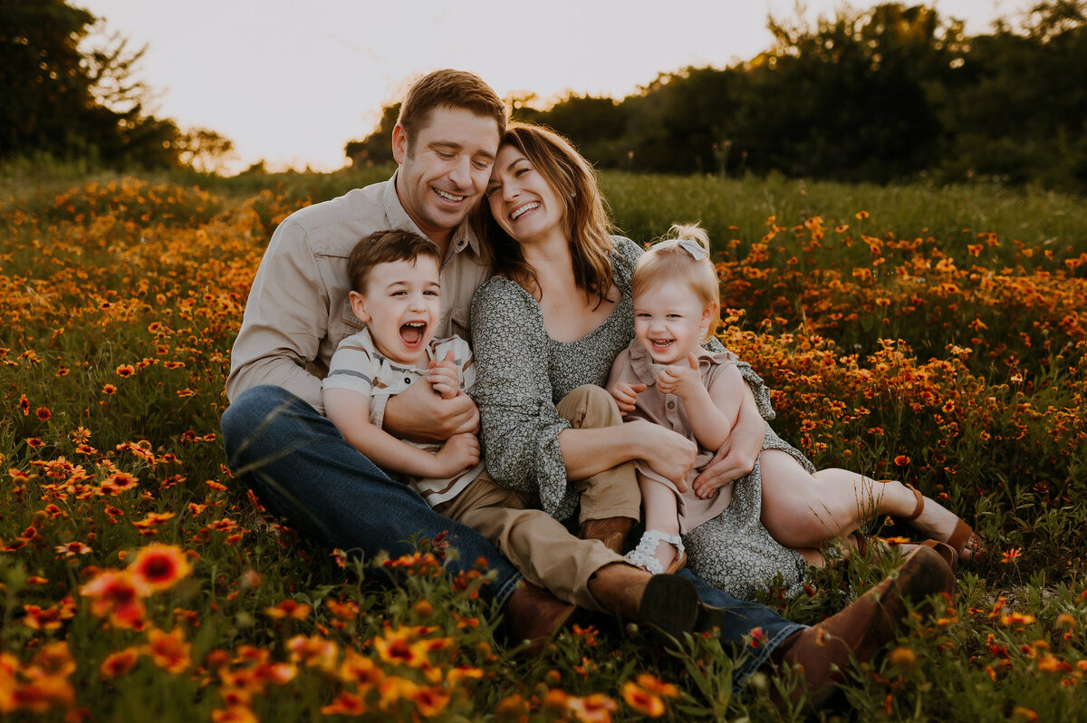 A family of four sitting in the middle of a wildflower field and giggling at Northwest Community Park in Fort Worth, Texas