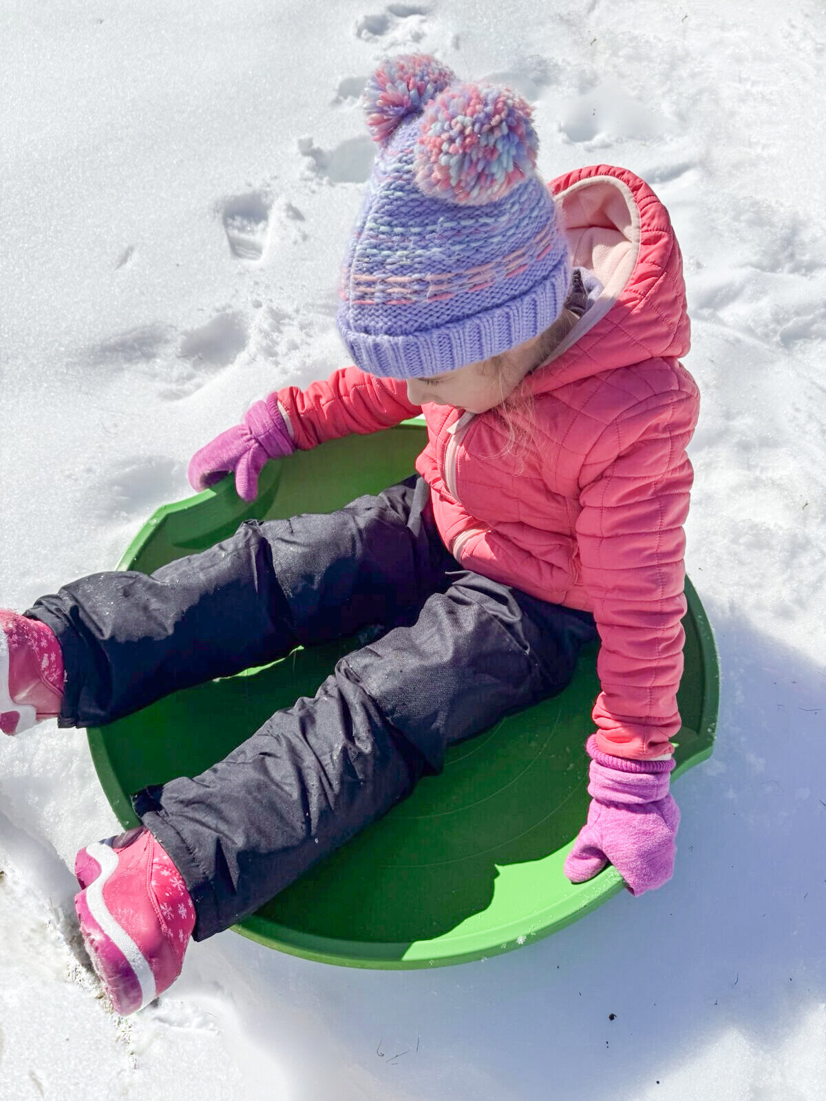 Student playing on sled in the snow covered outdoor play space at House of Parker Preschool in Gorham Maine. 