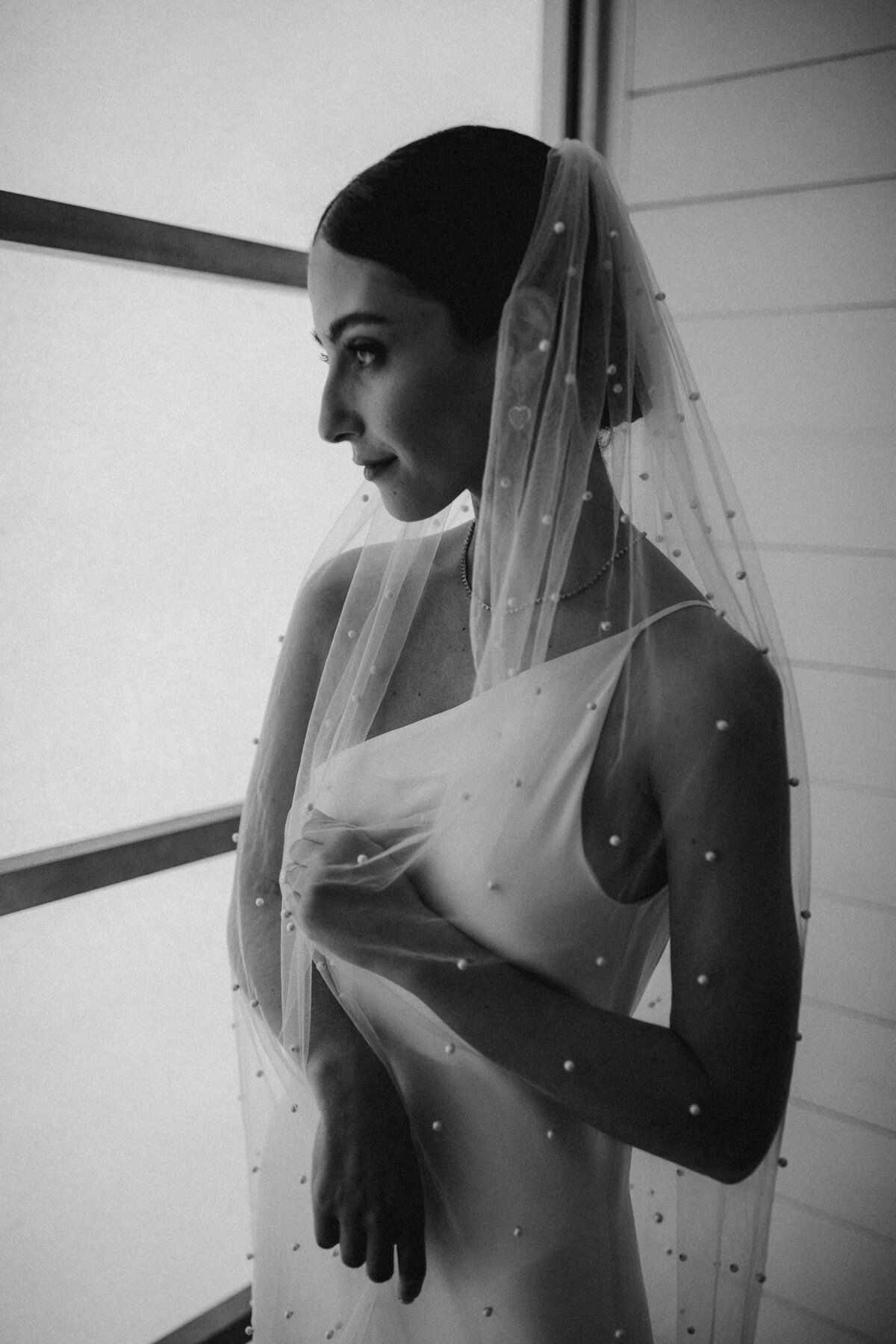 Bride wearing sleek white dress  with pearl embellishments on bridal veil